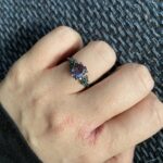 Nina’s hand wearing a purple gemstone ring, with natural skin texture visible.