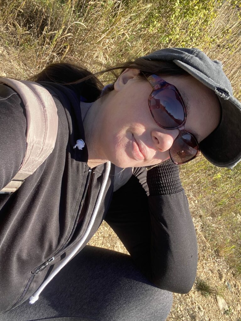 Nina resting outdoors in the sun, wearing sunglasses and a cap.
