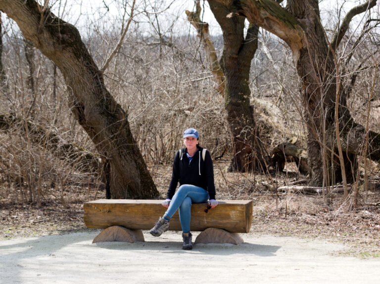 Nina sitting quietly on a fallen log in leafless woods.