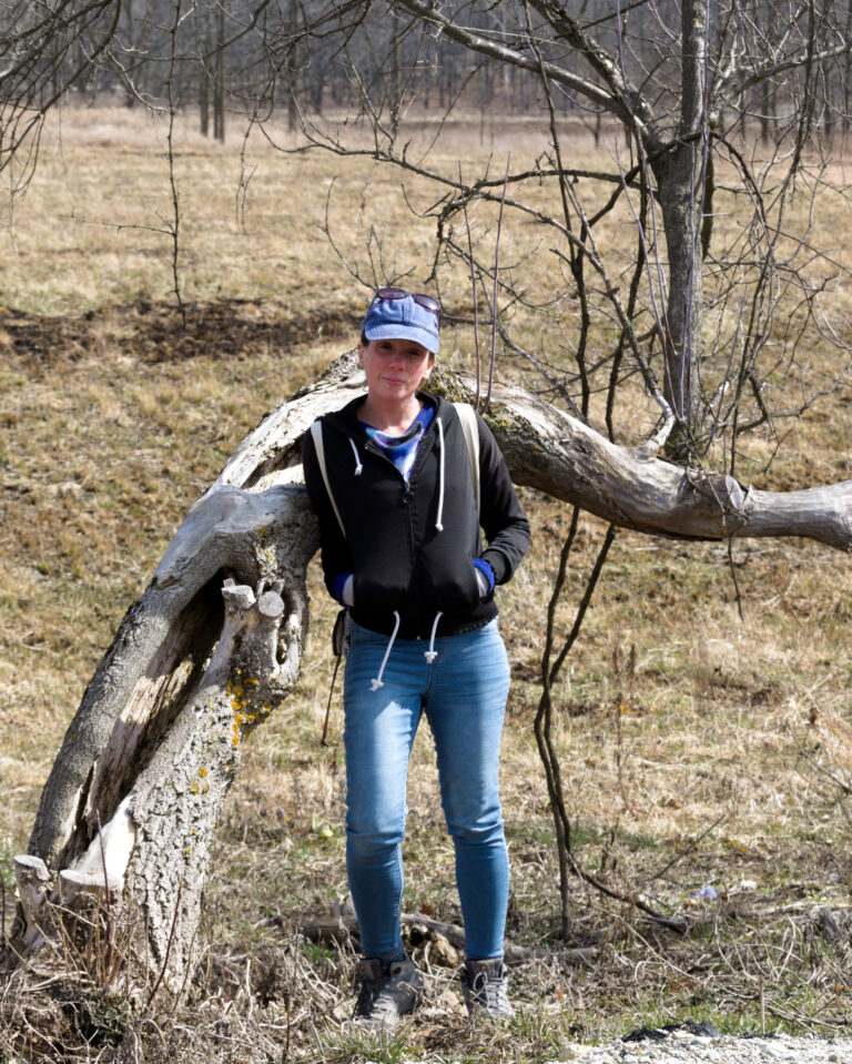 Nina standing beside a curved fallen tree in a quiet woodland.