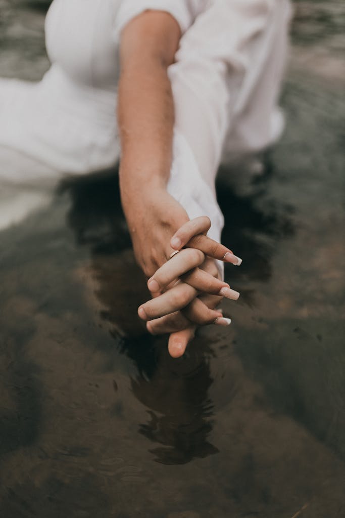 Close-up of a couple clasping hands above a serene pond, symbolizing connection and love.